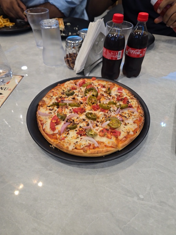 A loaded pizza with jalapeno, onion and tomato, served with cold drinks